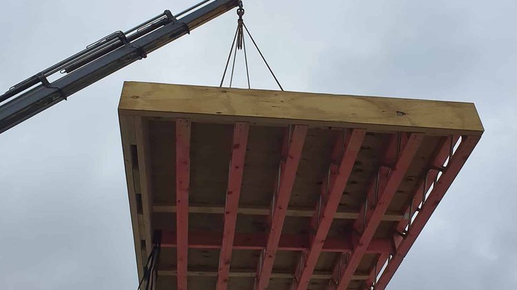 Waihi Passive House - Low camera angle of wall panel suspend from crane arm