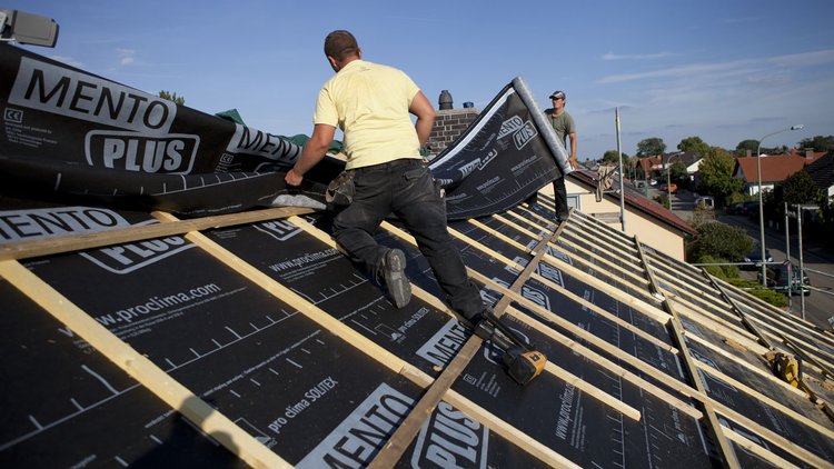 This photograph shows two roofing tradespeople installing SOLITEX Mento Plus membranes on a roof, against a background of a blue sky.