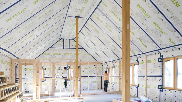 Two tradespeople installing INTELLO membranes inside the roof and walls of a bright house.