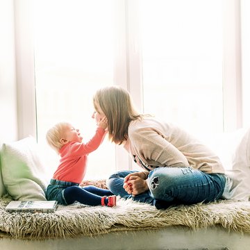 A photograph of a woman and a young child sitting on the window sill in a cosy home environment